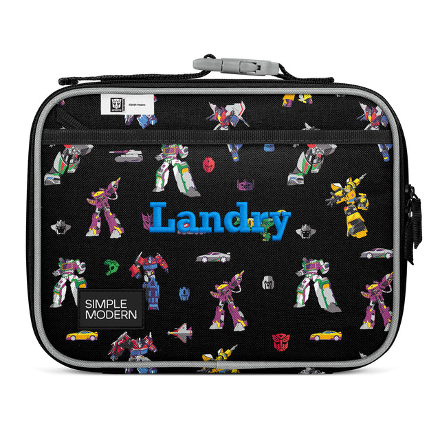 Black insulated Landry lunch box by Simple Modern featuring colorful Transformers characters, gray fabric handle, and side carry handles on white background. Black insulated Landry lunch box by Simple Modern featuring colorful Transformers characters, gray fabric handle, and side carry handles on white background.