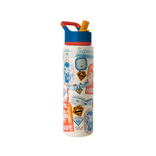 Simple Modern insulated water bottle with cream base, color-block red and blue top, and golden yellow spout cap. Features Superman-themed graphics including shields, 