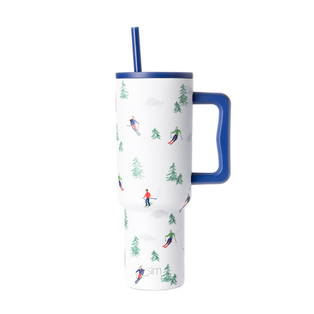 Insulated tumbler with cobalt blue lid and handle, white body, blue straw, featuring forest-themed green print design. Insulated tumbler with cobalt blue lid and handle, white body, blue straw, featuring forest-themed green print design.