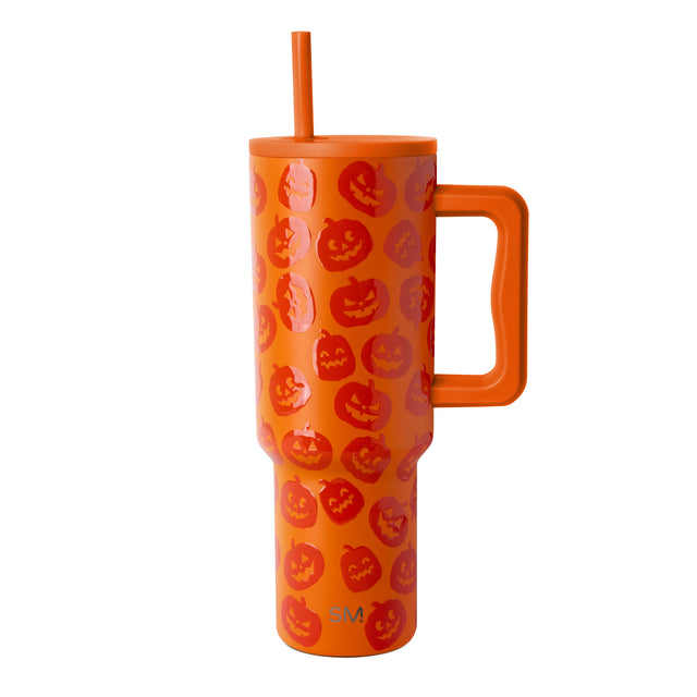 Bright orange tumbler with jack-o'-lantern faces in red, darker orange, and pink throughout, featuring a matching orange handle and straw. Bright orange tumbler with jack-o'-lantern faces in red, darker orange, and pink throughout, featuring a matching orange handle and straw.