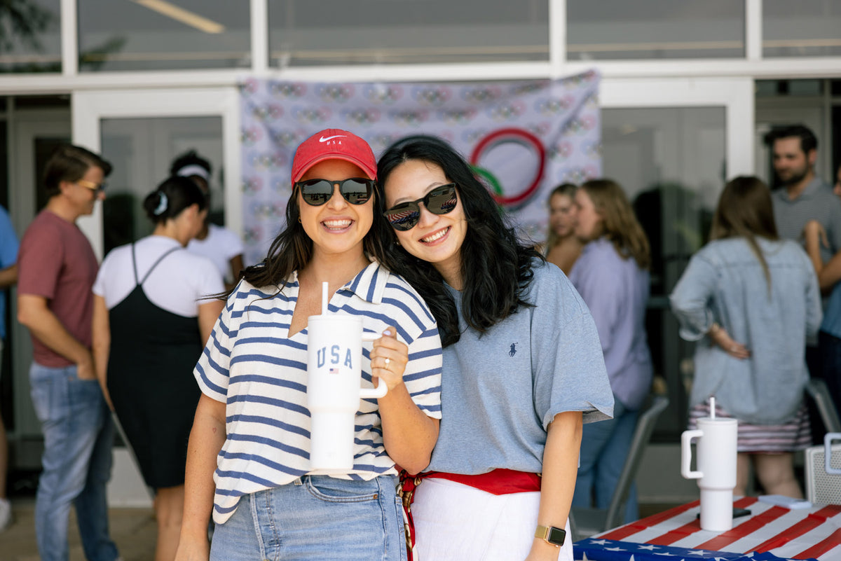 Two people smiling outdoors at an event, one holding a USA-themed tumbler.