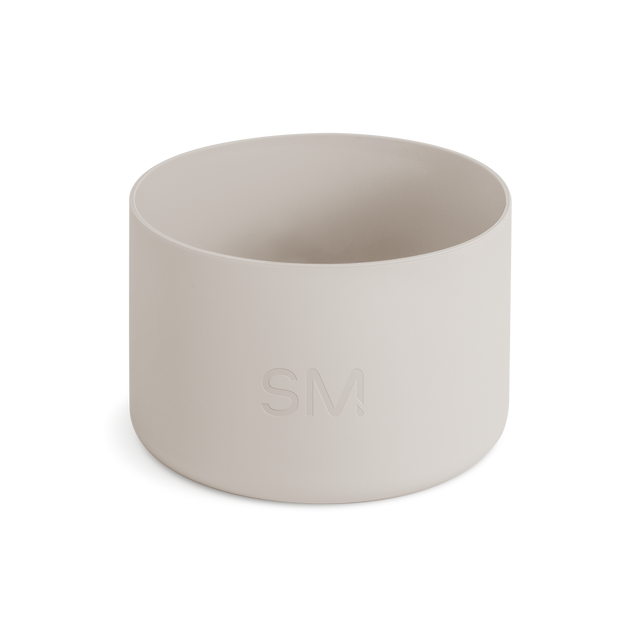 Off-white matte cylindrical boot product on pale beige background. Neutral, warm cream color palette with soft lighting.