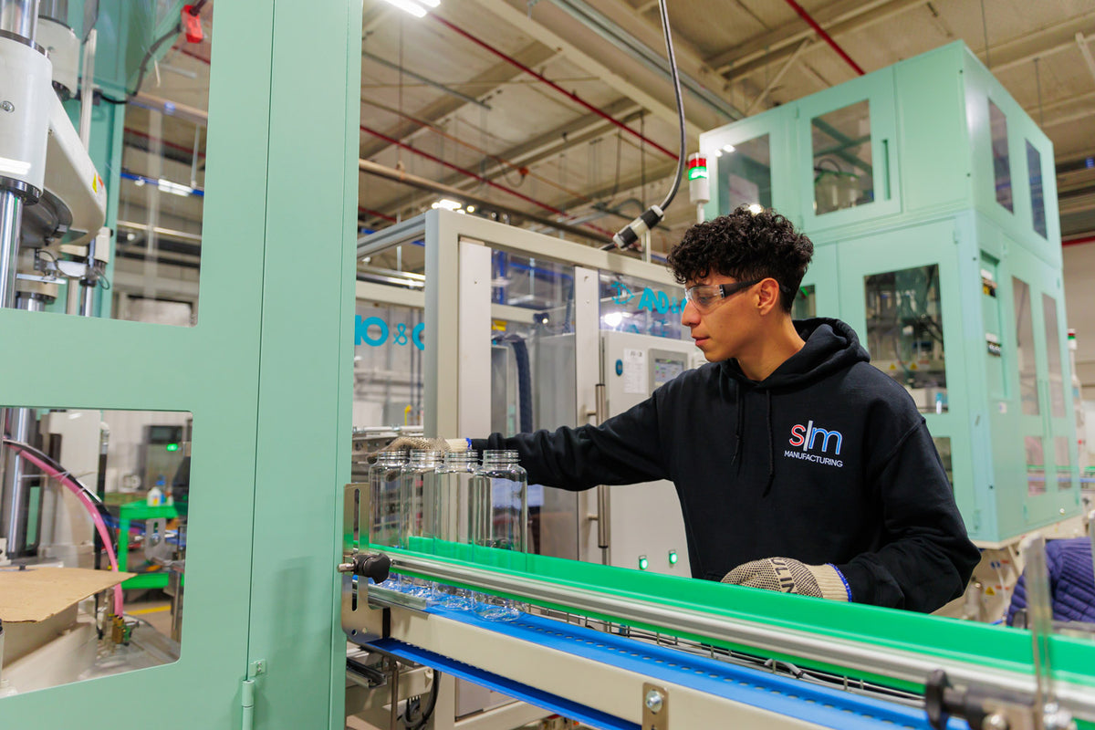 A Simple Modern team member handling tumbler bodies on a factory production line.