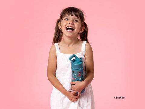 Young girl with long brunette hair smiling while holding a teal Disney Moana water bottle with colorful character artwork against a soft pink background.