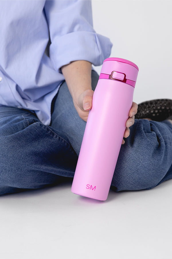 Person holding a bright pink water bottle against a soft periwinkle blue background outdoors.