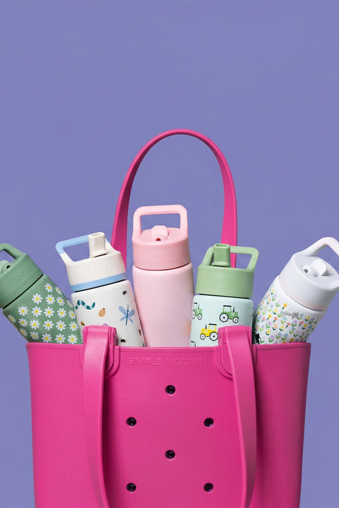 Hot pink Simple Modern tote bag filled with five colorful insulated drinkware bottles featuring daisy, botanical, tractor, and geometric patterns in green, white, pink, and mint green against a purple background.