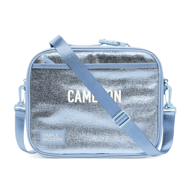 Simple Modern Cameron shoulder bag with silver metallic center panel and periwinkle blue handles, featuring top zippered closure and adjustable webbing strap against white background.