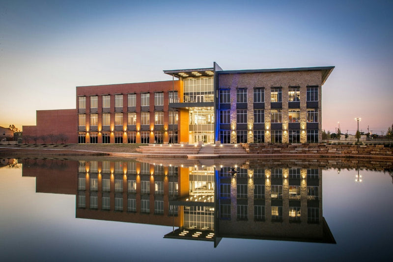 Modern brick and stone building facade illuminated by warm golden lighting at twilight, featuring deep red-brown tones and architectural details of a contemporary headquarters structure.