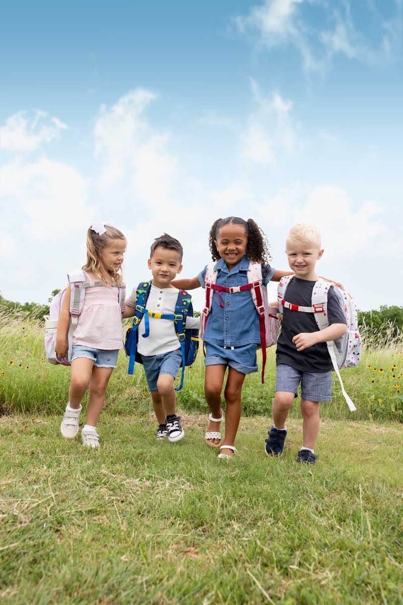 Four children wearing Simple Modern backpacks walking through a field.