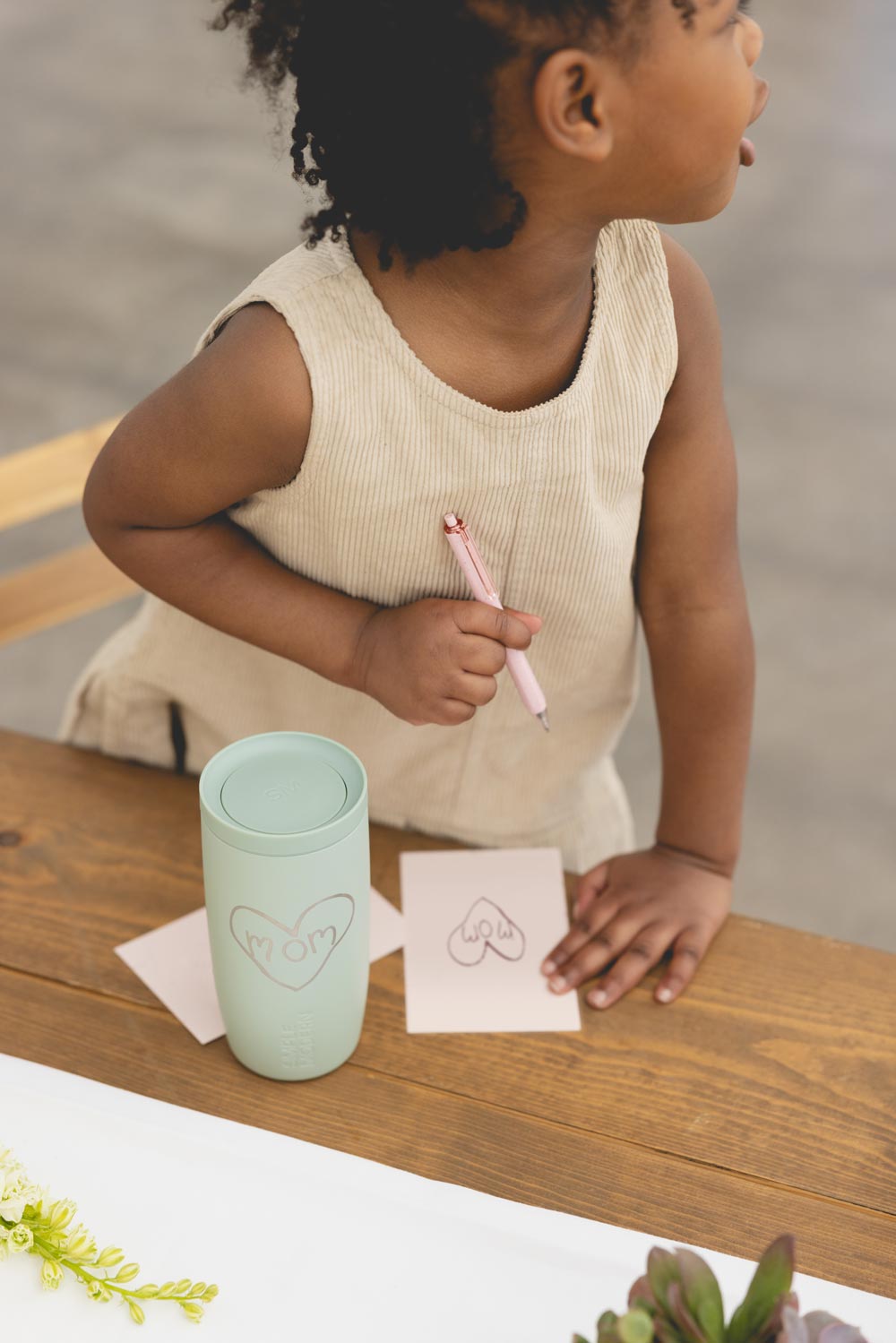 A child smiles up at their mother, who is holding a mint tumbler engraved with a heart and the word mom.
