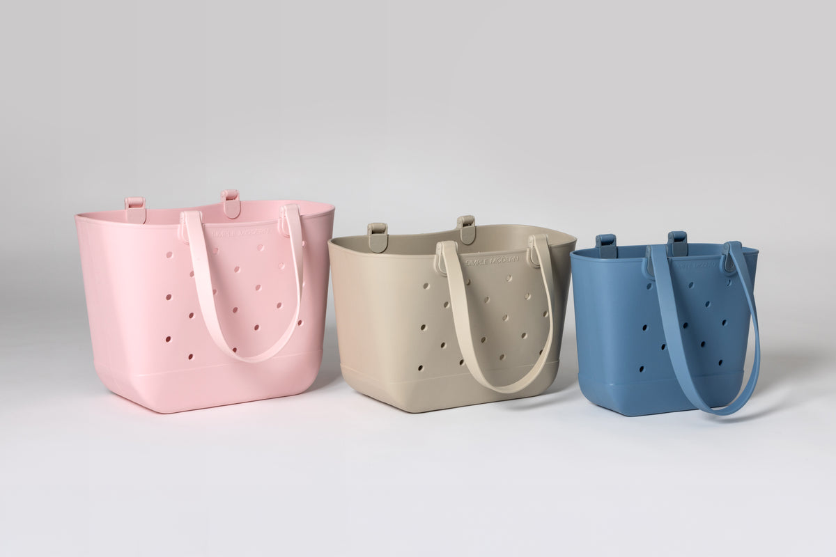 Three Getaway Bag totes in pink, sand and blue lined up largest to smallest to compare the three sizes.