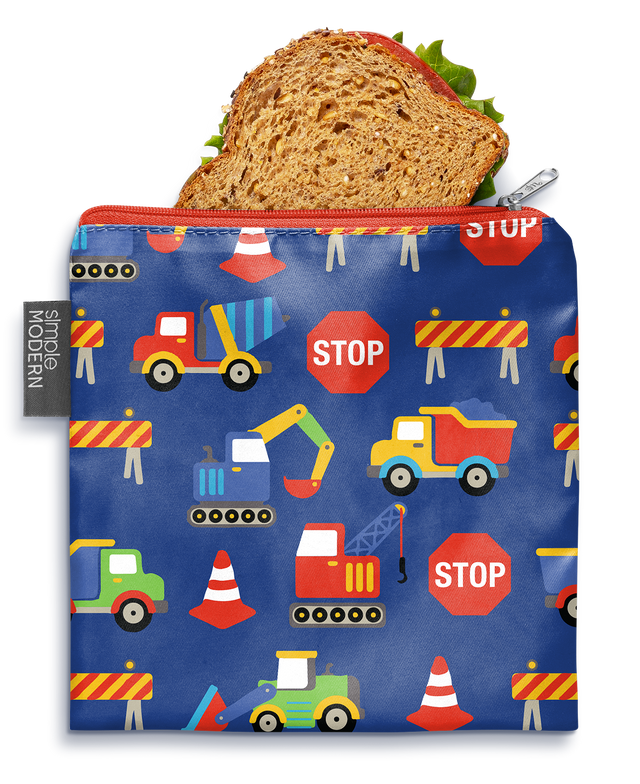 Colorful sandwich bag with royal blue background featuring bright red, yellow, lime green, and orange accents. Whole wheat bread slice with tan and cream tones visible in corner.